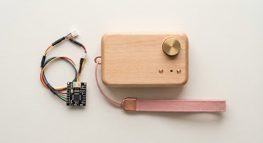 Wooden soundbox with a brass dial and pink strap, next to a small wired circuit board